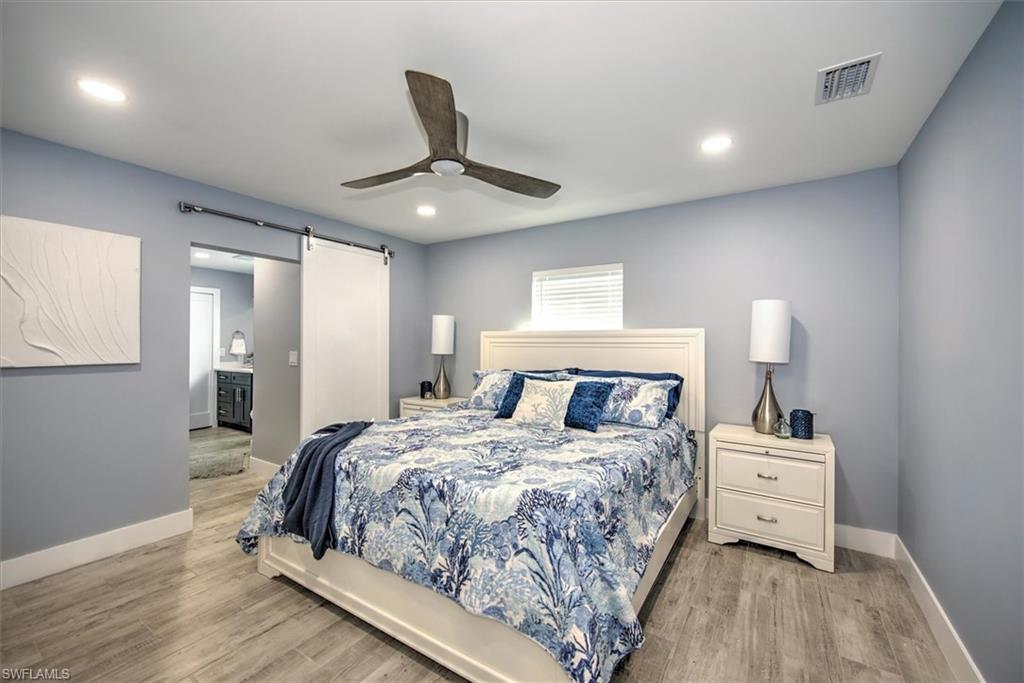 Bedroom featuring ceiling fan, light wood-type flooring, ensuite bathroom, and a barn door
