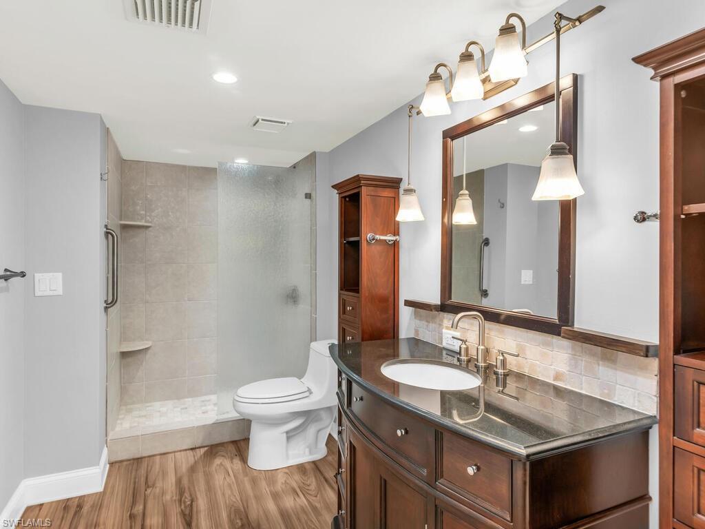 Bathroom featuring a tile shower, hardwood / wood-style flooring, toilet, vanity, and decorative backsplash