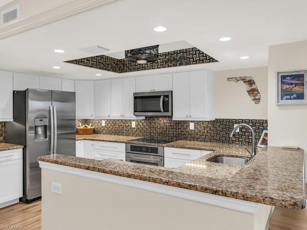 Kitchen with kitchen peninsula, stone countertops, appliances with stainless steel finishes, sink, and white cabinetry