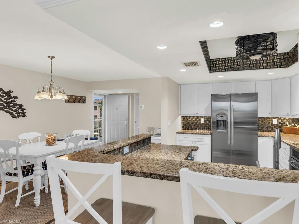 Kitchen featuring decorative light fixtures, white cabinetry, dark stone countertops, stainless steel fridge, and a breakfast bar area