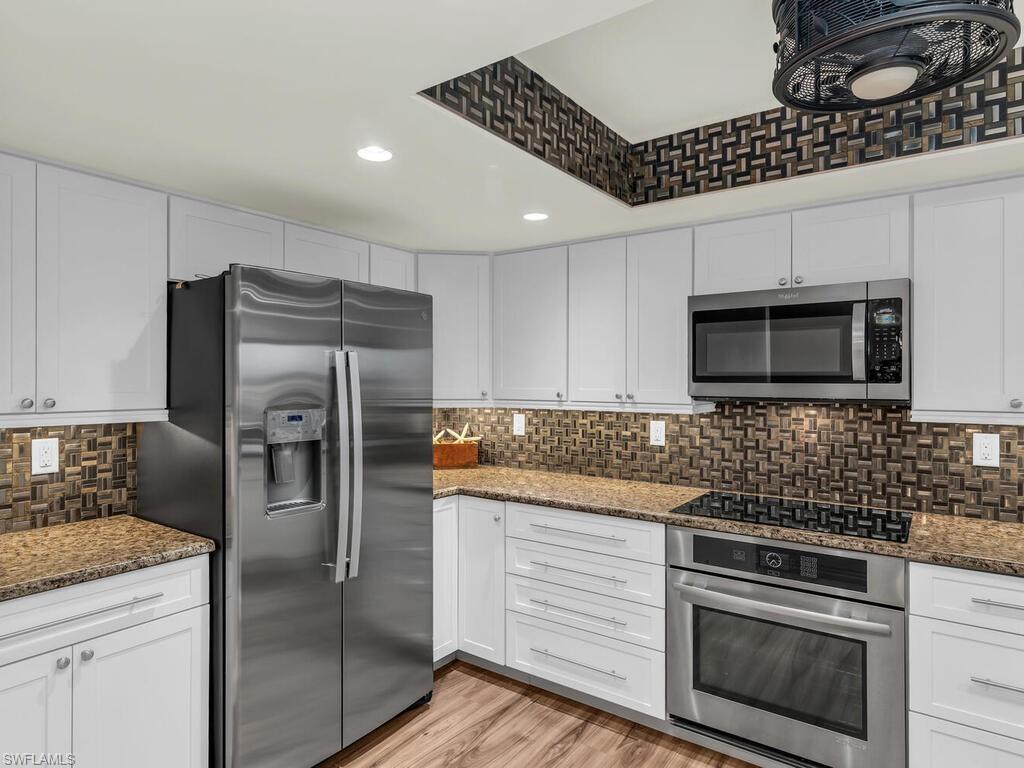 Kitchen with white cabinets, stainless steel appliances, dark stone countertops, and light hardwood / wood-style floors