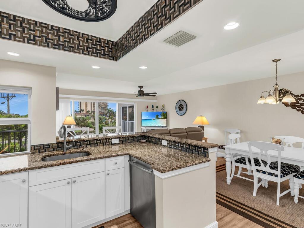 Kitchen with stainless steel dishwasher, white cabinets, kitchen peninsula, and dark stone counters