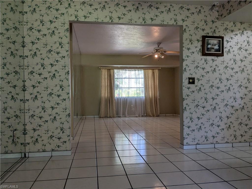 Spare room with wallpapered walls, light tile patterned flooring, and a ceiling fan