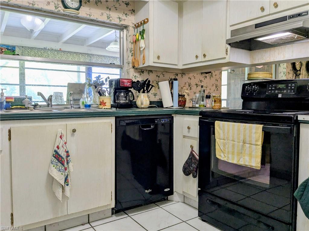 Kitchen with black appliances, under cabinet range hood, white cabinets, light tile patterned flooring, and plenty of natural light