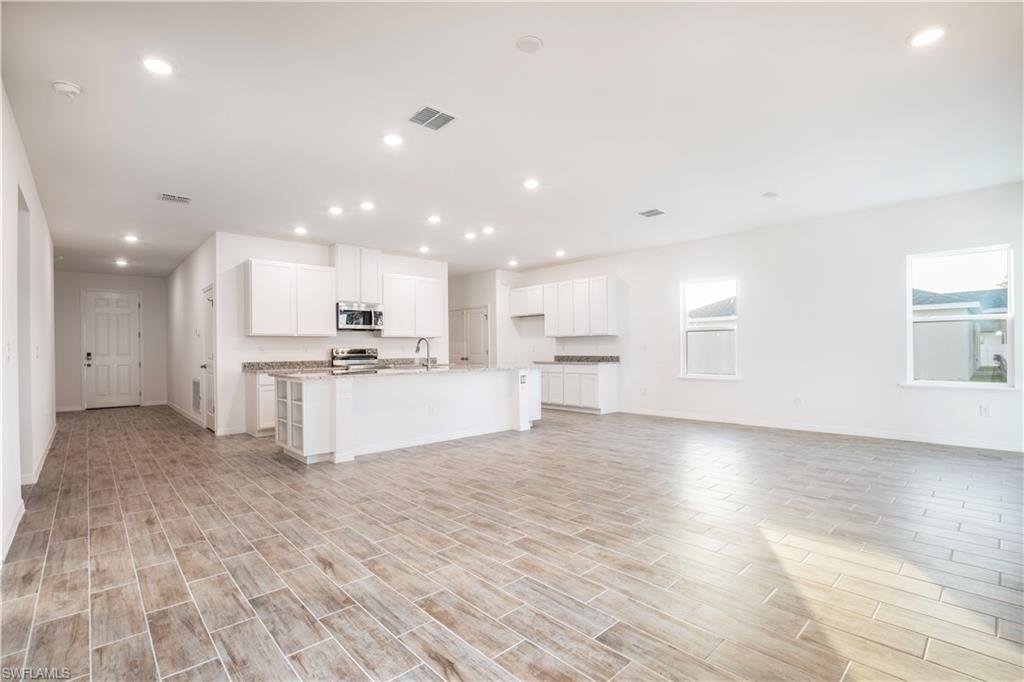 Kitchen featuring white cabinets, wood finish floors, a kitchen island with sink, open floor plan, and recessed lighting