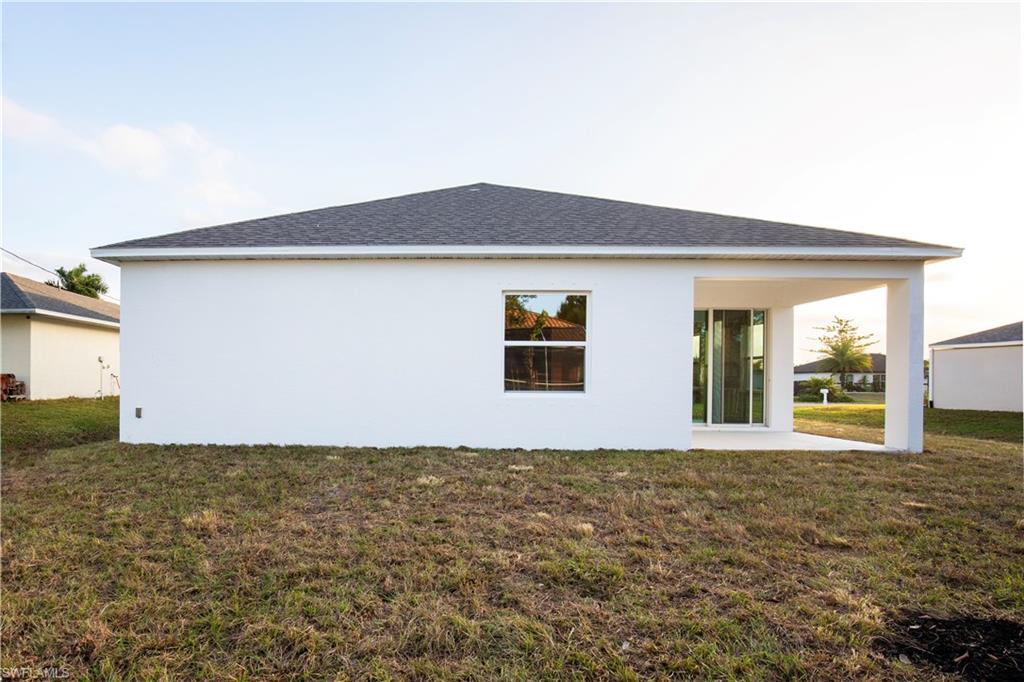 Back of house with stucco siding, a lawn, and a shingled roof