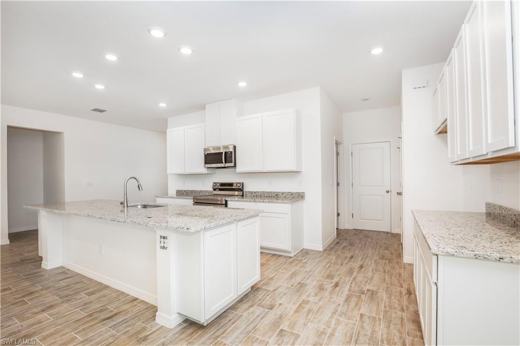 Kitchen featuring wood tiled floors, white cabinets, light stone countertops, appliances with stainless steel finishes, and recessed lighting