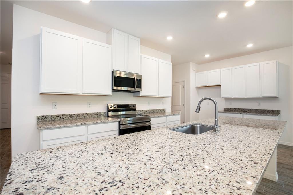 Kitchen featuring stainless steel appliances, wood finish floors, white cabinets, light stone countertops, and recessed lighting