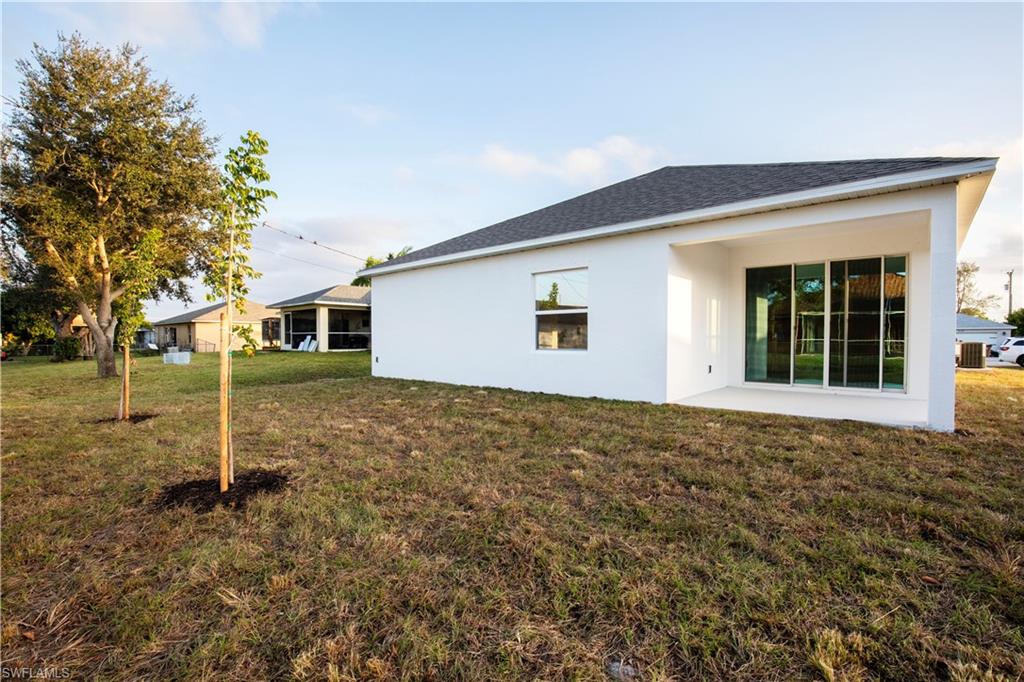 Back of property with stucco siding, a lawn, roof with shingles, and a patio