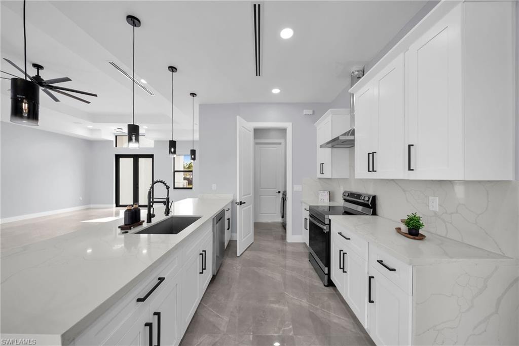 Kitchen featuring decorative light fixtures, white cabinets, light stone counters, and stainless steel appliances