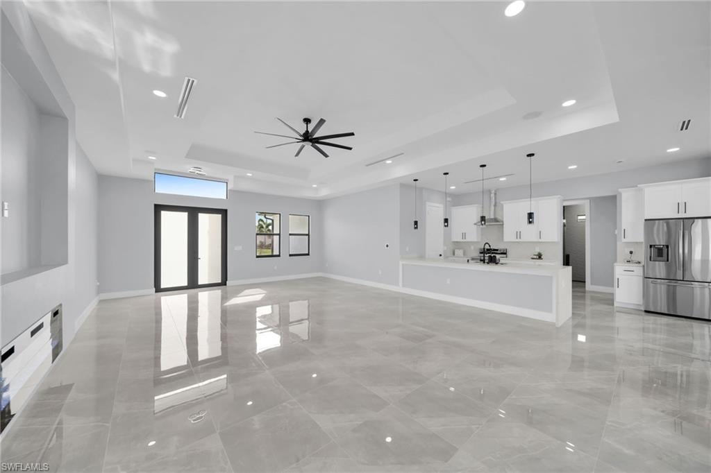 Unfurnished living room with ceiling fan, sink, and a tray ceiling