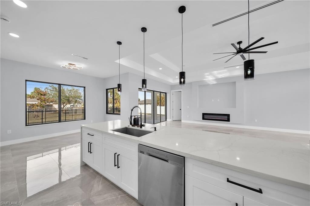 Kitchen featuring light stone countertops, white cabinets, sink, hanging light fixtures, and stainless steel dishwasher