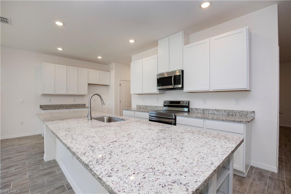 Kitchen with stainless steel appliances, white cabinets, wood tiled floors, light stone counters, and recessed lighting