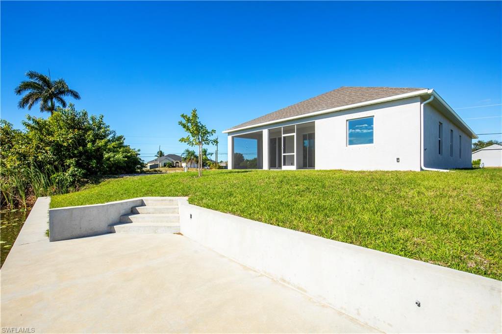 Back of house with a yard, stucco siding, a sunroom, and roof with shingles