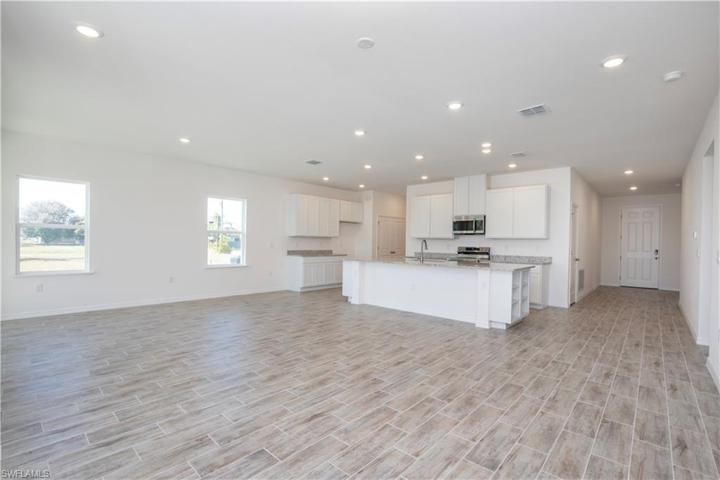 Kitchen with wood tiled floors, white cabinetry, an island with sink, open floor plan, and stainless steel appliances