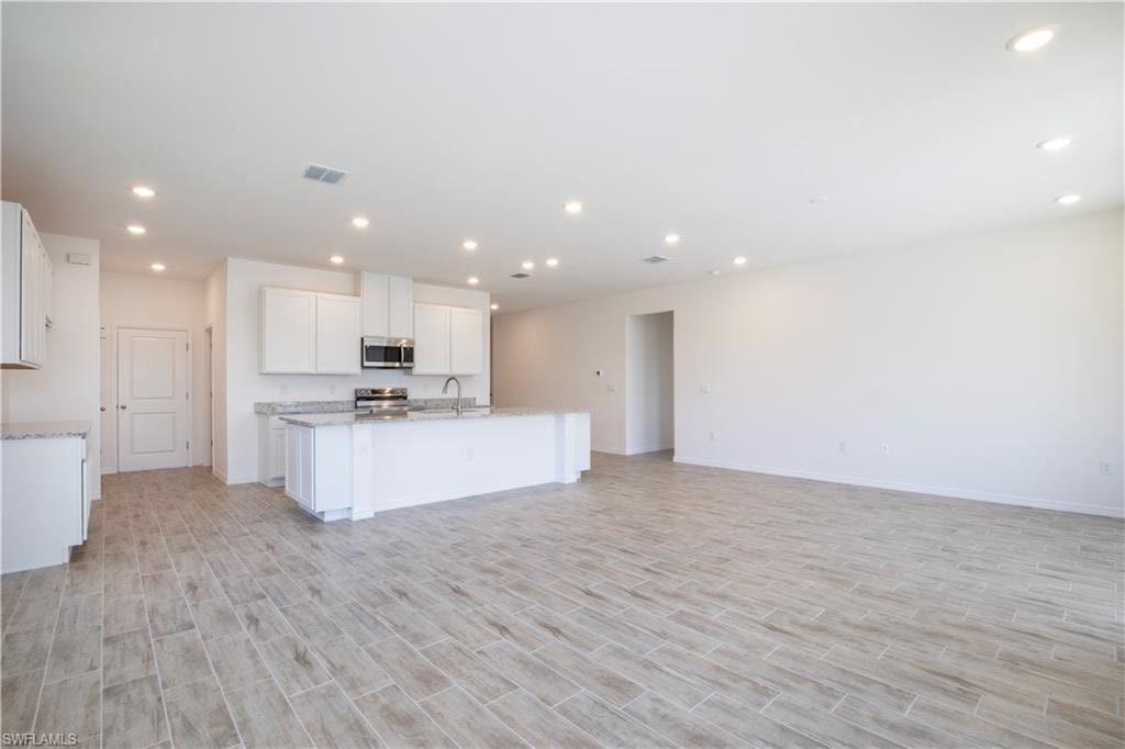 Kitchen with white cabinetry, recessed lighting, open floor plan, wood finish floors, and stainless steel appliances