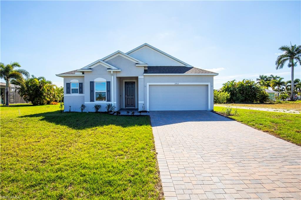 View of front facade featuring a front lawn, decorative driveway, a garage, and stucco siding