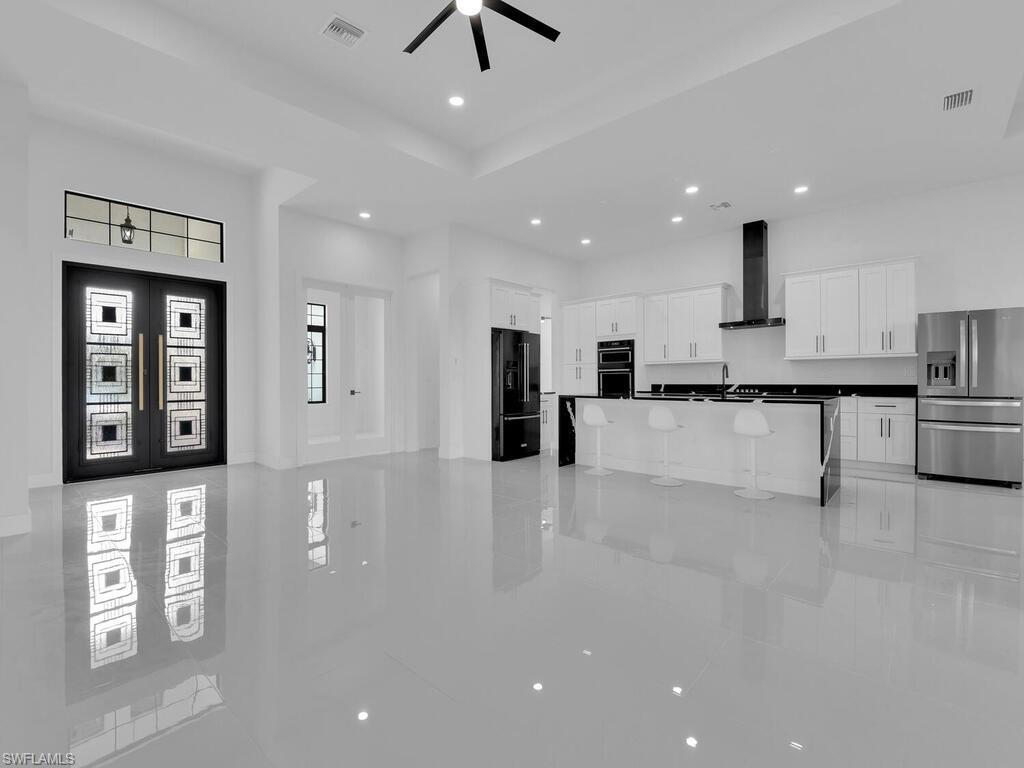 Kitchen with white cabinetry, ceiling fan, wall chimney range hood, black appliances, and a center island