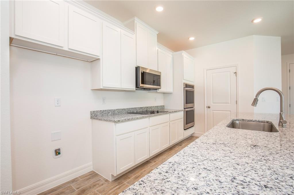 Kitchen with light stone counters, wood tiled floors, white cabinetry, and recessed lighting