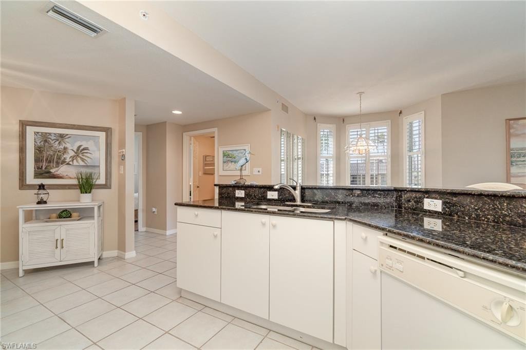 Kitchen with decorative light fixtures, dishwasher, sink, white cabinets, and dark stone counters