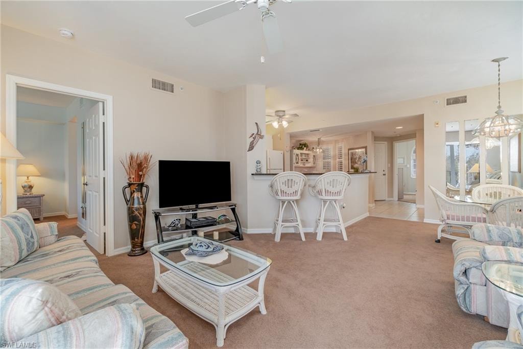 Living room with ceiling fan with notable chandelier and light colored carpet