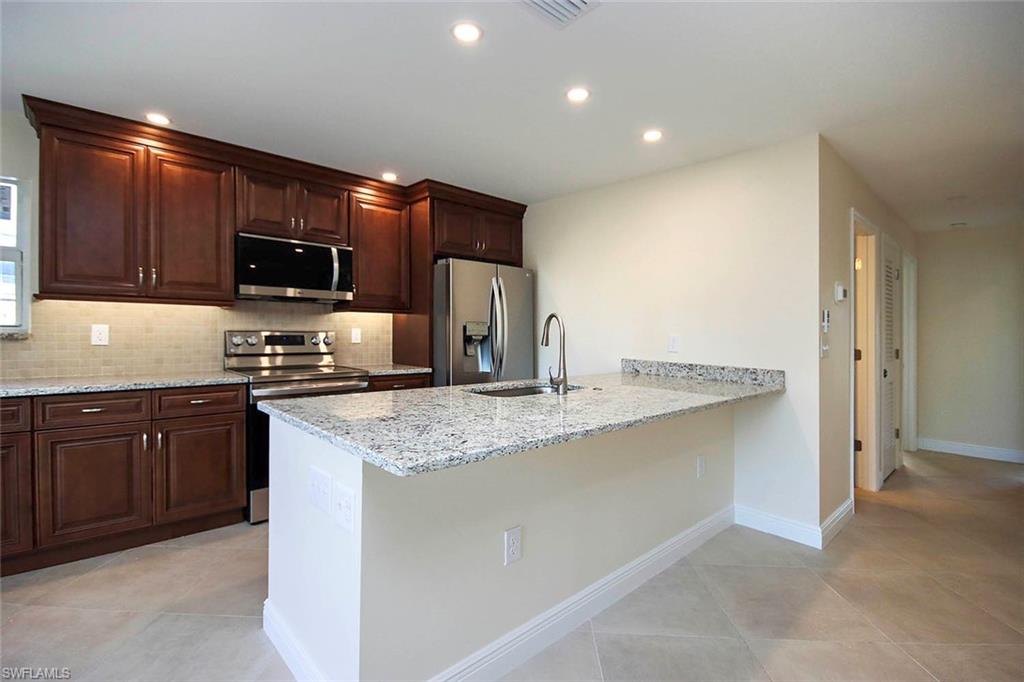 Kitchen with appliances with stainless steel finishes, sink, kitchen peninsula, light stone counters, and light tile patterned floors