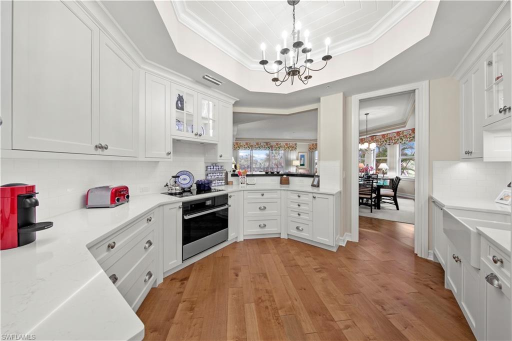 Kitchen with stainless steel oven, tasteful backsplash, hanging light fixtures, white cabinets, and an inviting chandelier