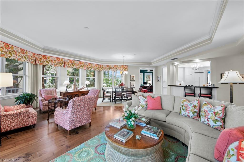 Living room featuring wood-type flooring, a tray ceiling, crown molding, and a chandelier