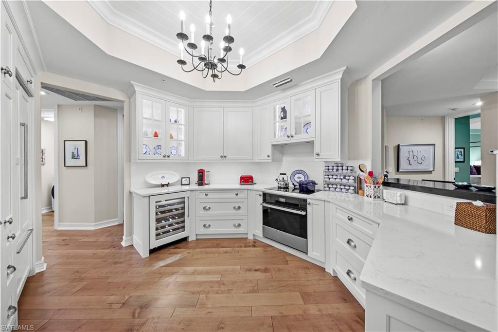 Kitchen with beverage cooler, white cabinetry, hanging light fixtures, stainless steel oven, and crown molding