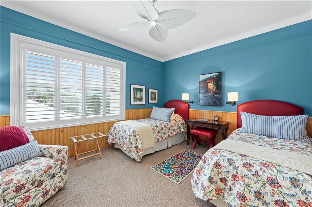 Carpeted bedroom featuring wood walls, ceiling fan, and ornamental molding