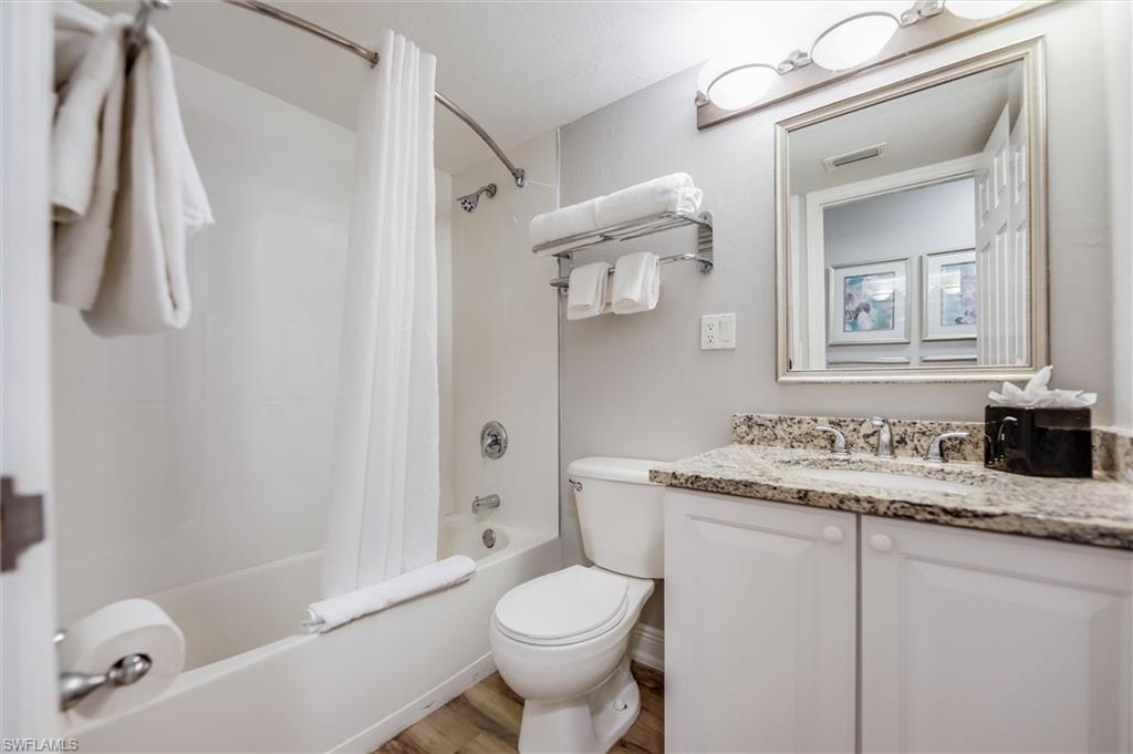 Full bathroom with vanity, hardwood / wood-style floors, toilet, and shower / bath combo with shower curtain