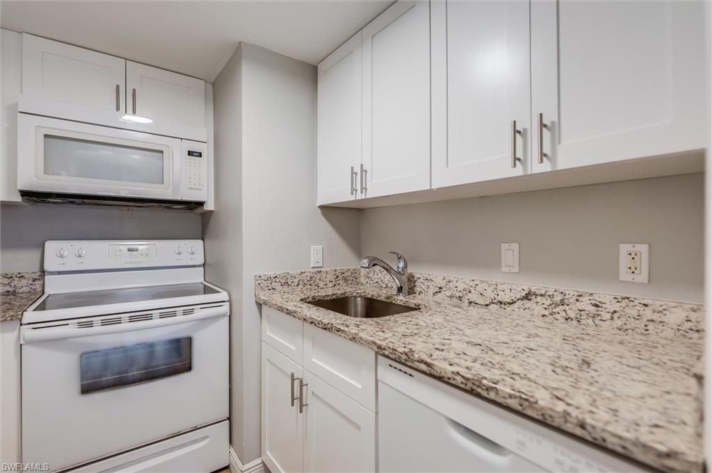 Kitchen featuring white cabinetry, light stone countertops, sink, and white appliances