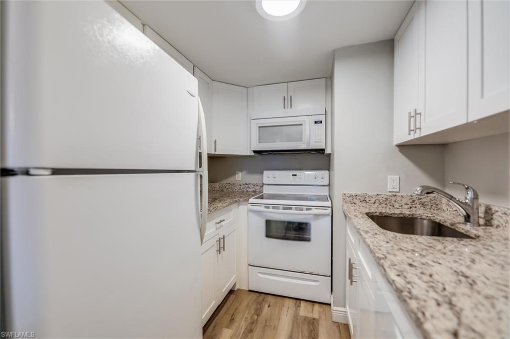 Kitchen with white cabinetry, white appliances, light stone countertops, and sink