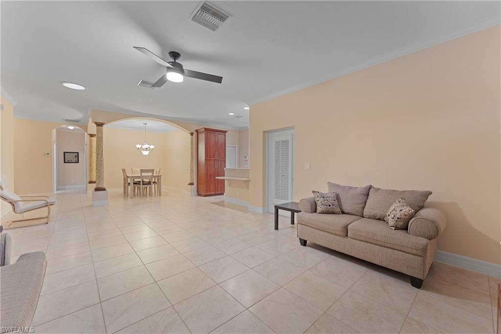 Tiled living room with crown molding and ceiling fan with notable chandelier