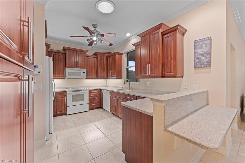 Kitchen with a kitchen bar, kitchen peninsula, white appliances, ornamental molding, and sink