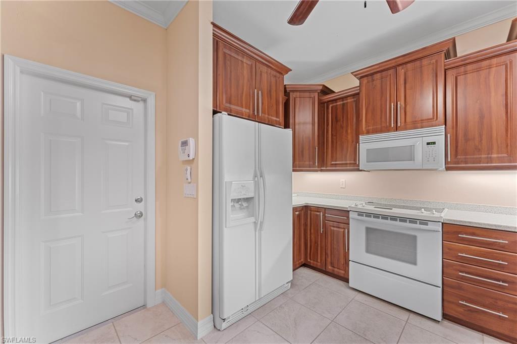 Kitchen with ceiling fan, white appliances, light tile patterned floors, and crown molding