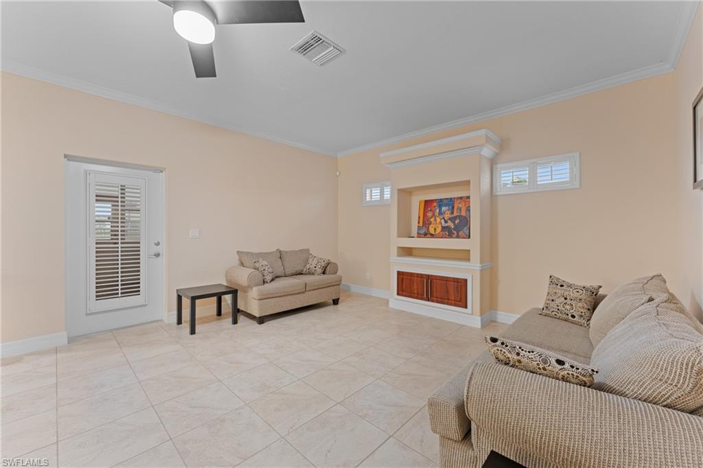Living room with ceiling fan, built in shelves, light tile patterned floors, and crown molding