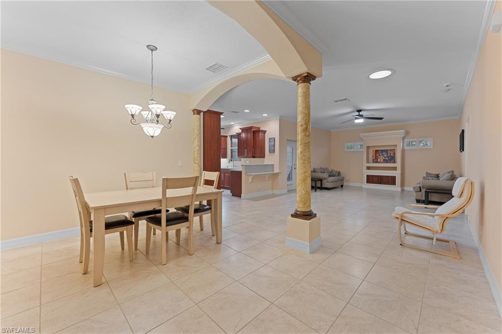 Dining space with light tile patterned floors, ceiling fan with notable chandelier, ornamental molding, and ornate columns