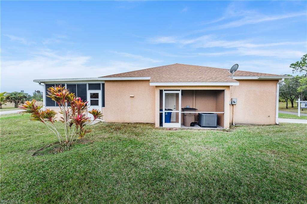 Back of property featuring a lawn, central AC unit, and a sunroom