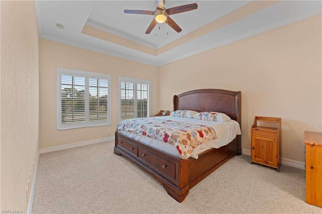 Carpeted bedroom with ceiling fan, crown molding, and a raised ceiling