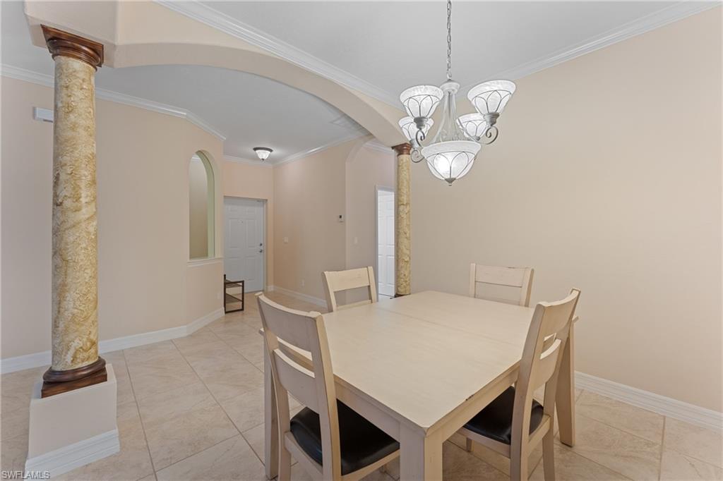Tiled dining area with decorative columns, crown molding, and a notable chandelier