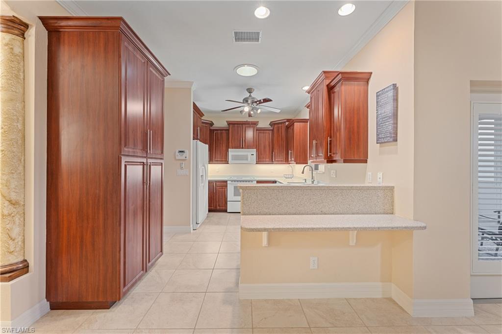 Kitchen with light tile patterned floors, kitchen peninsula, white appliances, and ornamental molding