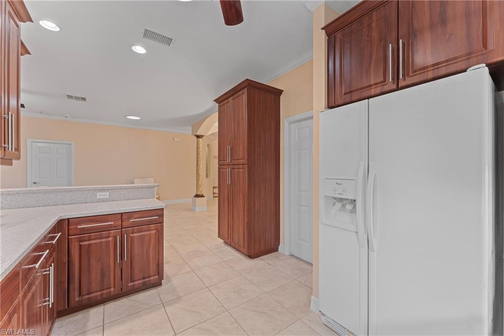 Kitchen with light tile patterned floors, ceiling fan, white fridge with ice dispenser, light stone countertops, and ornamental molding