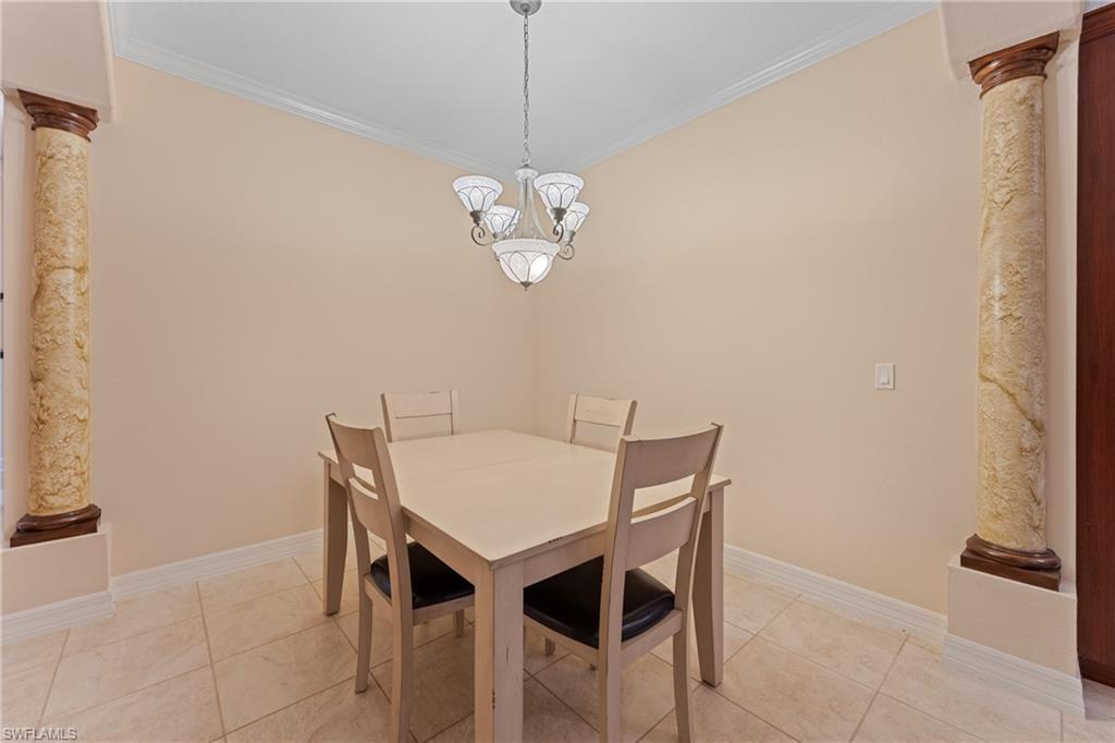 Dining room with light tile patterned floors, a notable chandelier, ornamental molding, and ornate columns
