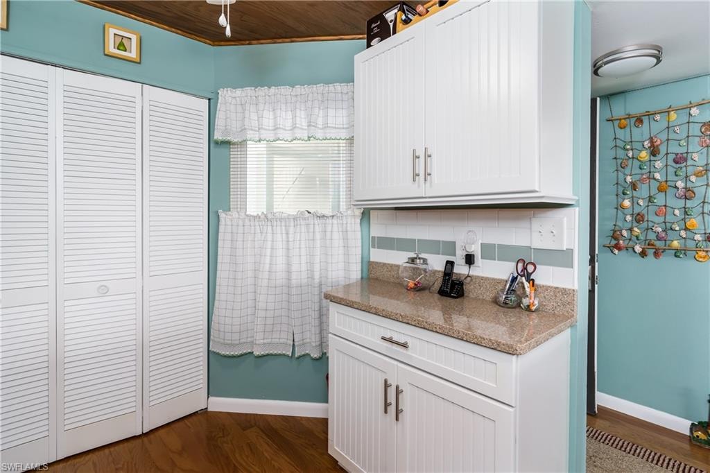 Kitchen with light stone countertops, white cabinets, wood flooring and ceiling, and tasteful backsplash