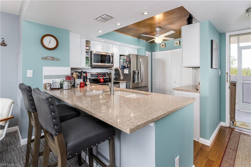 Kitchen with decorative backsplash, white cabinets, appliances with stainless steel finishes, and kitchen peninsula