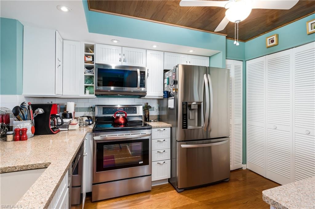Kitchen with white cabinets, tasteful backsplash, light wood flooring, and appliances with stainless steel finishes
