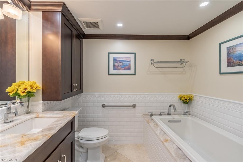 Guest Bathroom featuring vanity, tiled tub, crown molding, tile patterned flooring, and toilet