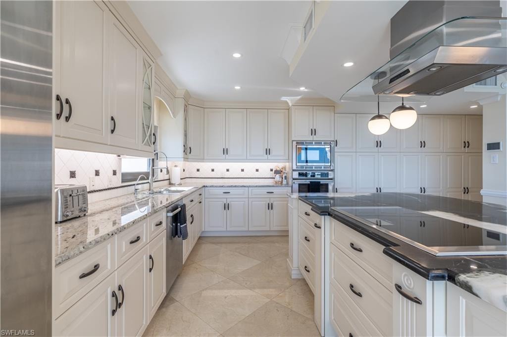 Kitchen featuring built in appliances, sink, white cabinets, island range hood, and decorative backsplash