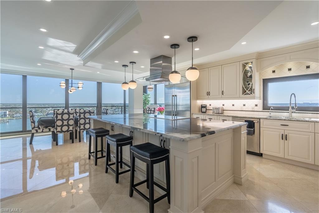 Kitchen with a large island, stainless steel appliances, light stone countertops, pendant lighting, and sink